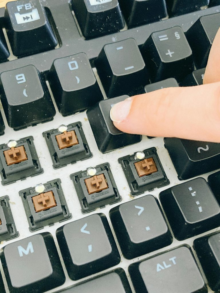 Detailed view of a finger pressing a key on a mechanical keyboard with exposed switches.